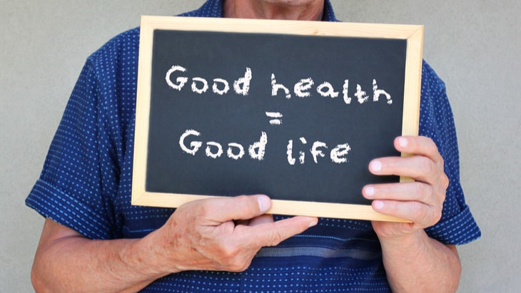 ‹man holding balckboard: good health, good life